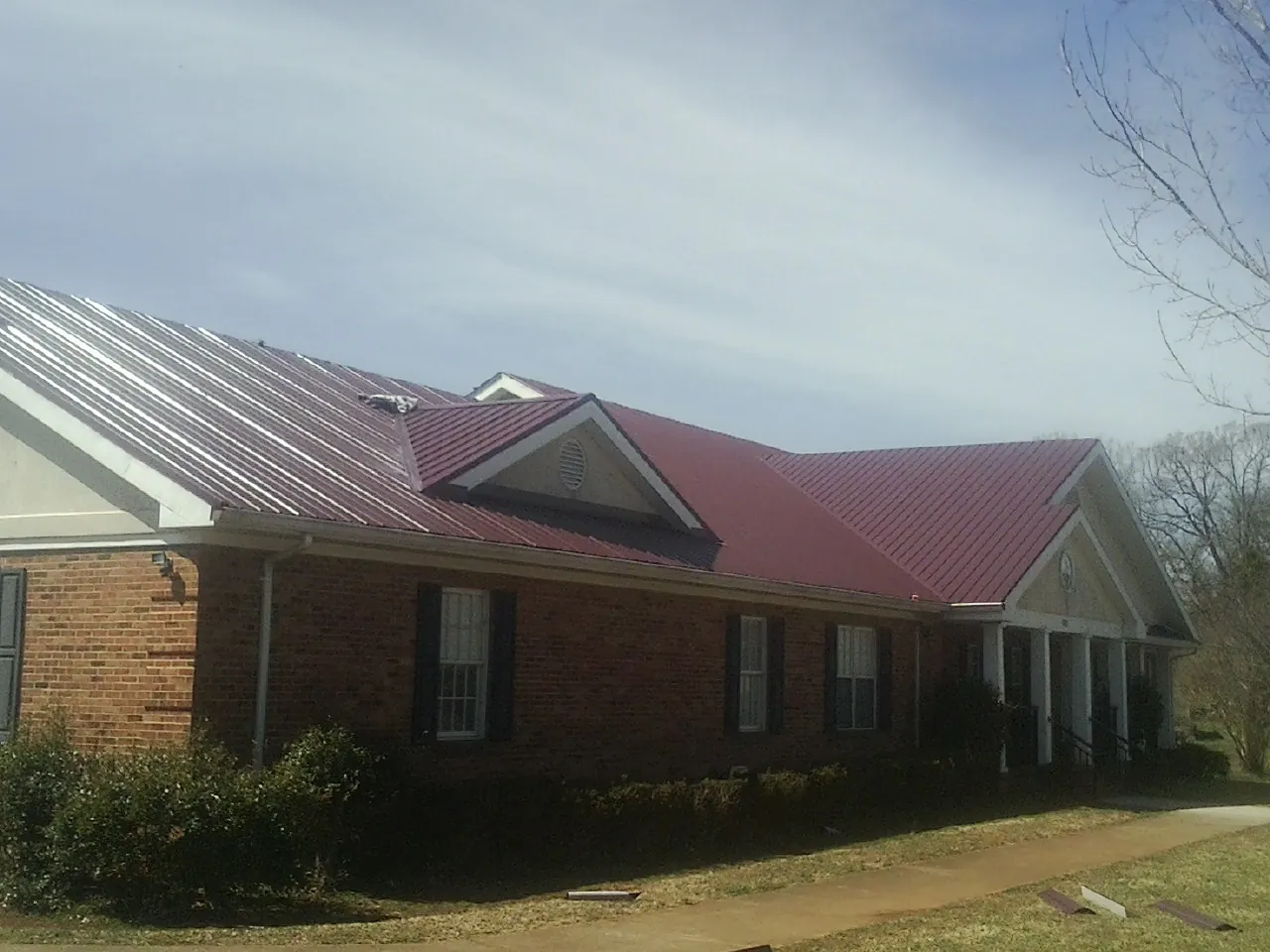 Red metal roof with gabled entries on a long brick building, from a Hail Damage Roof Repair job in Mchenry