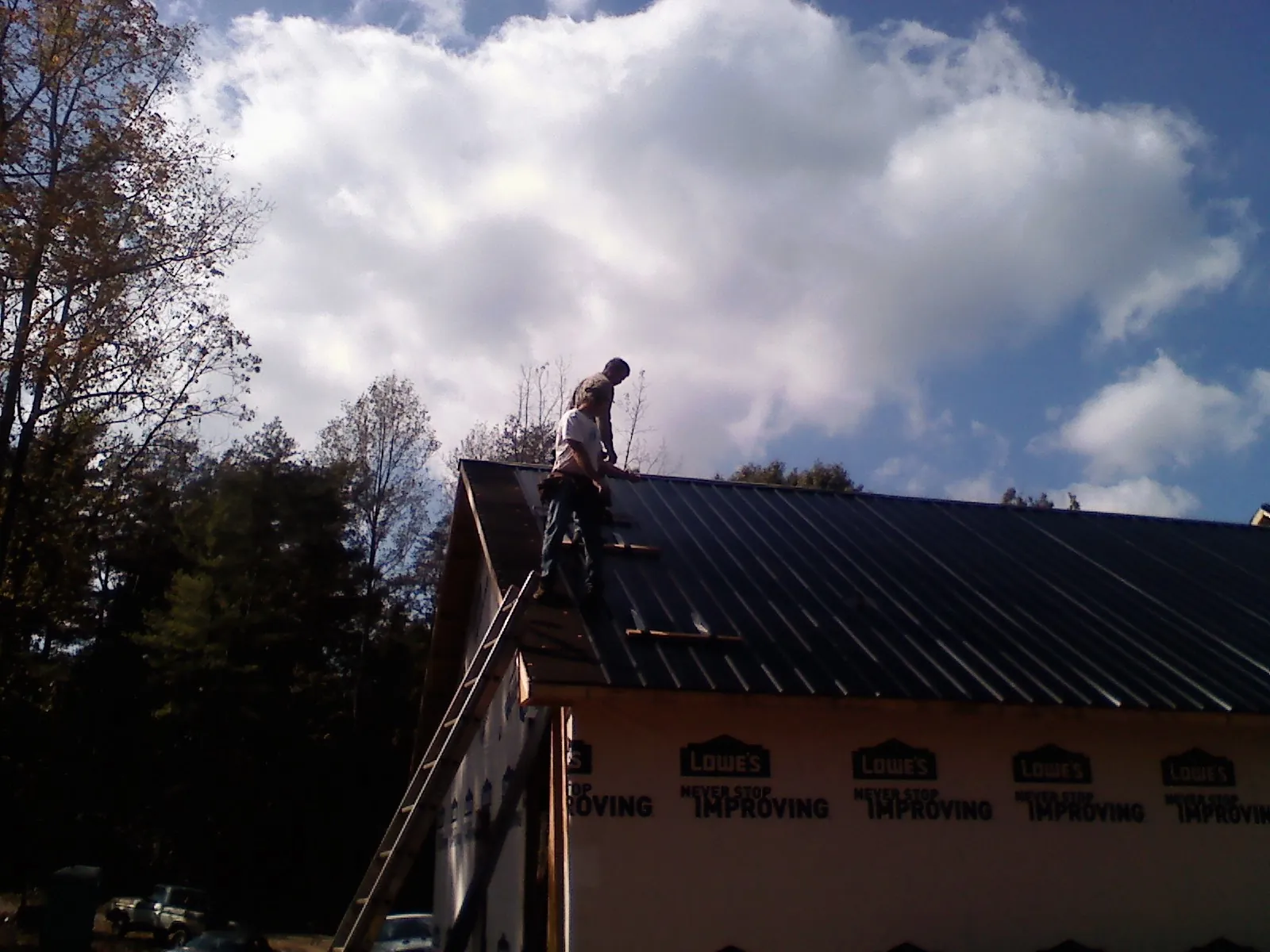 Roofer fastening dark metal panels high against a cloudy sky, from a Roof Inspection job in Mchenry
