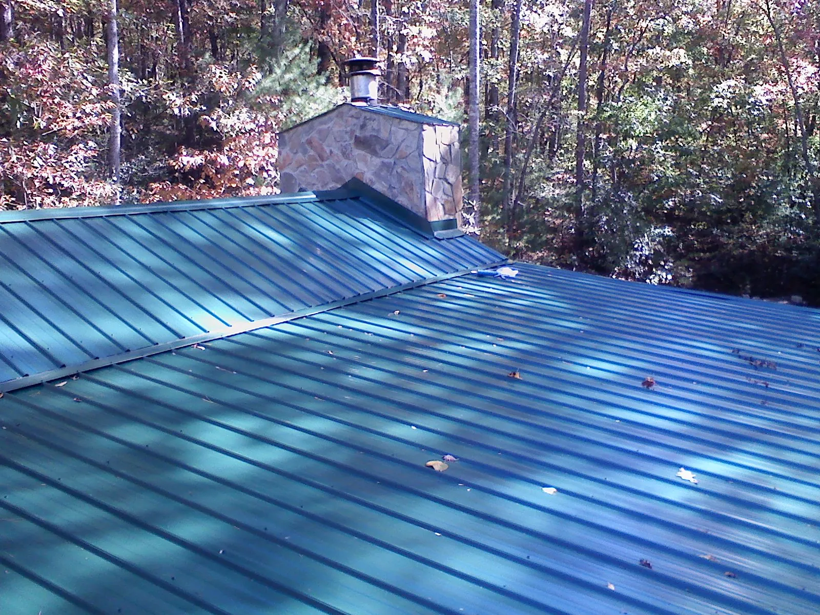 New green metal roof and stone chimney surrounded by autumn woods in Mchenry