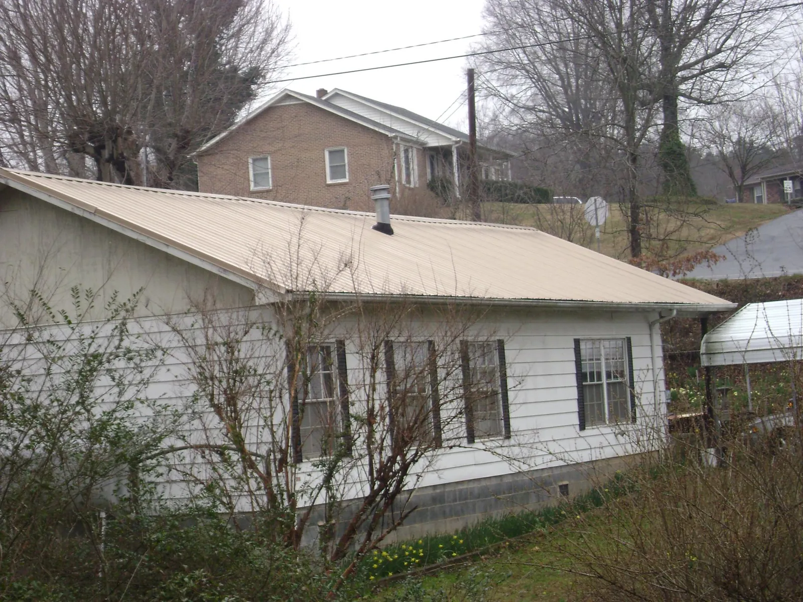 Tan metal roof on a white sided house set into a hillside — Commercial Roofing by Roofing Brothers in Mchenry